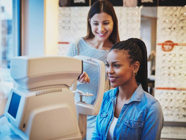 Beautiful young black woman wearing jean shirt sits at machine waiting to get eye exam