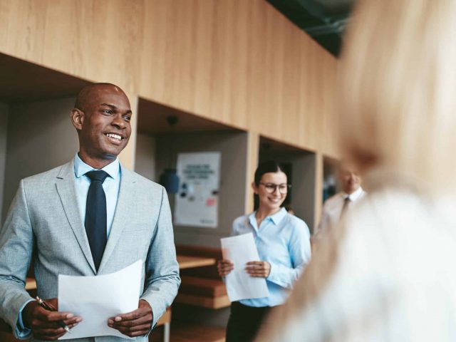 Smiling African American businessman walking with colleagues in Smiling African American businessman standing in an office holding paperwork after a meeting with a diverse group of colleagues